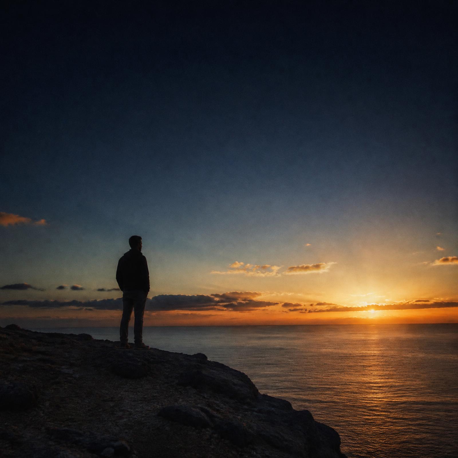 Silueta de un hombre solo en un acantilado mirando el horizonte al atardecer